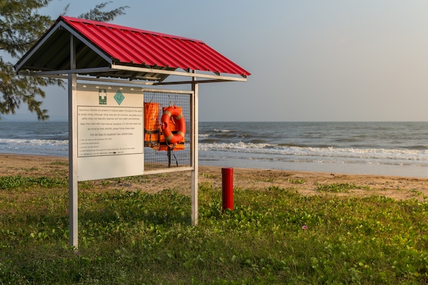 Coletes salva-vidas laranja pendurado em um rack com etiqueta de aviso para primeiros socorros em fundo de praia