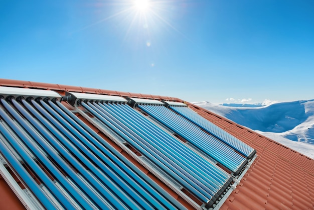 Foto coletores de vácuo - tubos de aquecimento solar de água no telhado da casa com montanhas de sol e neve