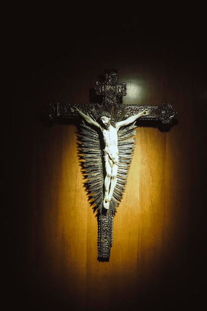 El colgante de la crucifixión de Jesús cuelga en una pared de madera marrón con un punto de luz para la cruz crucificada.