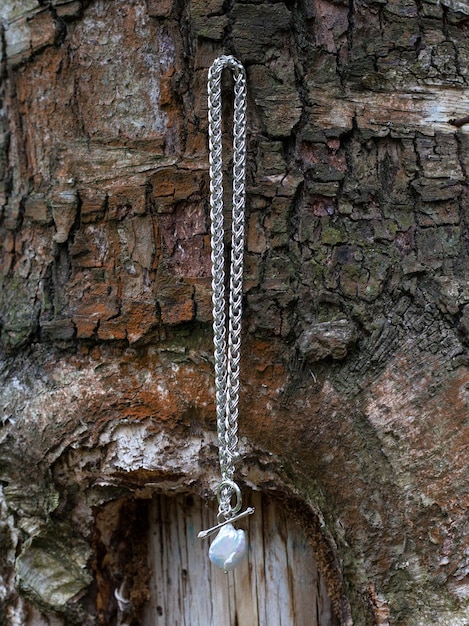 Colgante de perlas barrocas con cadena de plata sobre fondo de naturaleza de madera marrón