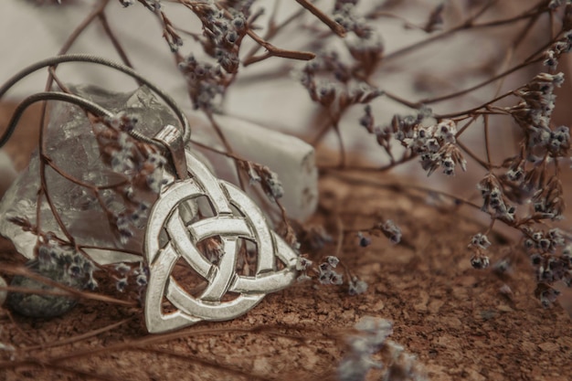 Colgante triquetra de plata sobre mesa de madera en flores secas