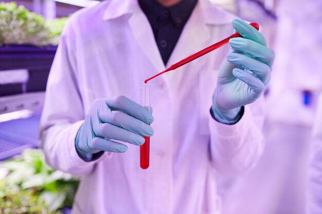 Colheita da seção intermediária de um cientista irreconhecível segurando um tubo de vidro com um líquido vermelho enquanto trabalha no laboratório biológico, copie o espaço