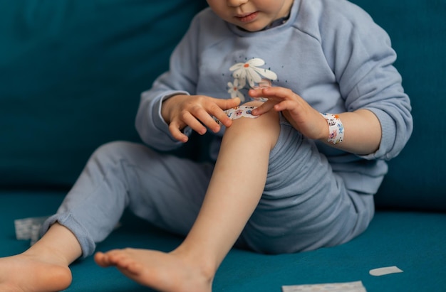 Colheita de criança cola um curativo na ferida nos joelhos Bebê menina usando cola azul no remendo com