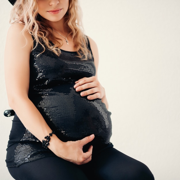 Colheita de mulher loira grávida no topo espumante elegante, abraçando sua barriga.