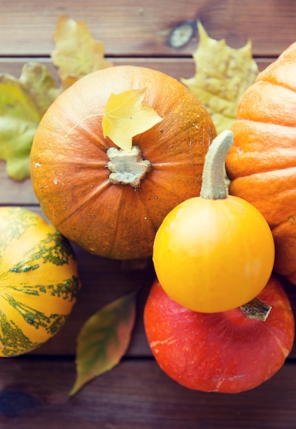 colheita, temporada, propaganda e conceito de outono - close-up de abóboras e folhas na mesa de madeira em casa