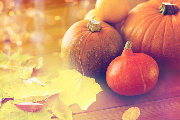colheita, temporada, propaganda e conceito de outono - close-up de abóboras e folhas na mesa de madeira em casa