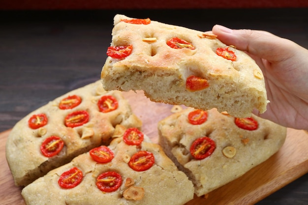 Colhendo manualmente uma fatia de pão italiano de focaccia de tomate e alho delicioso recém-assado