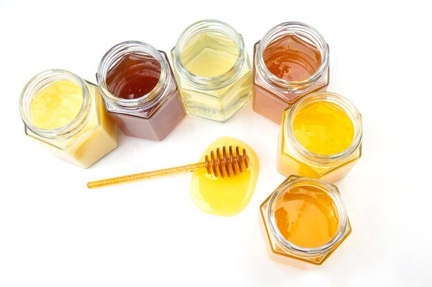 Colher com mel fresco e potes com diferentes tipos de mel em um fundo branco. alimentos vitamínicos orgânicos
