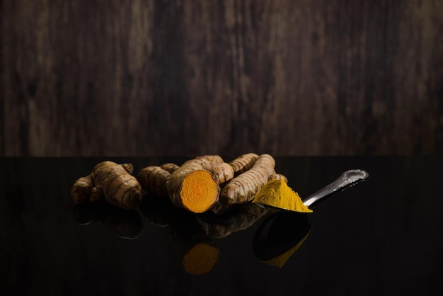 Colher com raízes de curcuma e açafrão na mesa preta com fundo de madeira