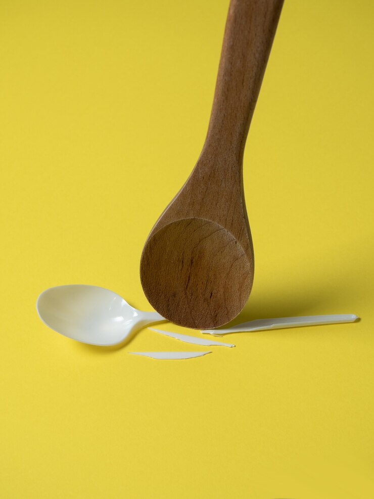 Foto colher de pau quebra uma colher descartável de plástico em um fundo amarelo. sem plástico