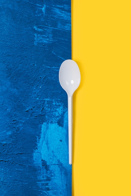 Colher descartável de plástico branco em um fundo clássico azul e amarelo