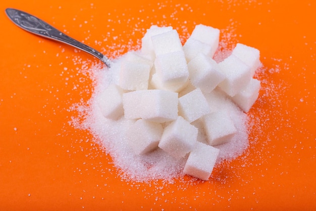 Colher e cubos de açúcar branco e açúcar granulado em um fundo laranja