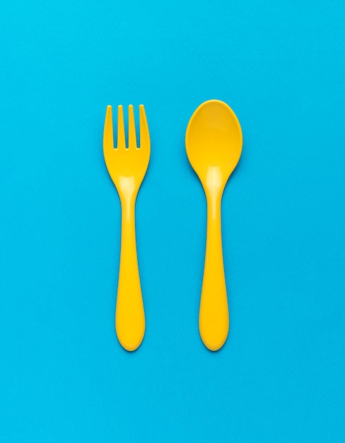 Colher e garfo de plástico amarelo brilhante sobre fundo azul Conjunto de alimentos de plástico Postura plana
