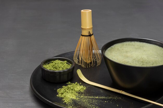 Colher medidora e pó de chá matcha matcha chá verde em uma tigela e um batedor de bambu em um prato preto