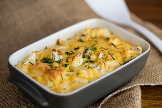 coliflor al horno con filete de pollo y verduras cubierto con queso en un molde de cerámica