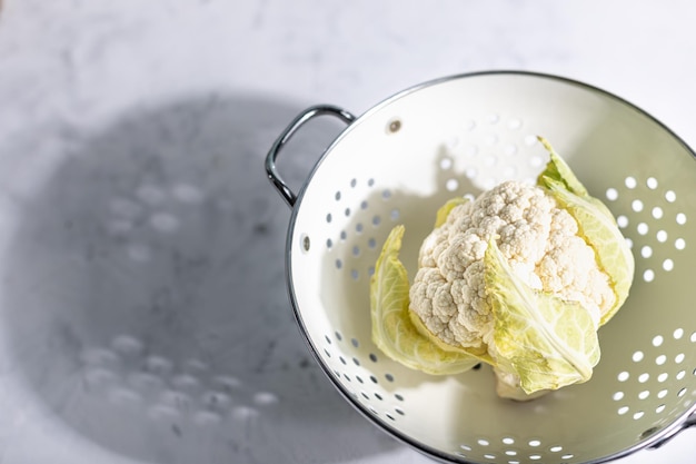 Coliflor fresca en un colador sobre un fondo blanco con sombras duras