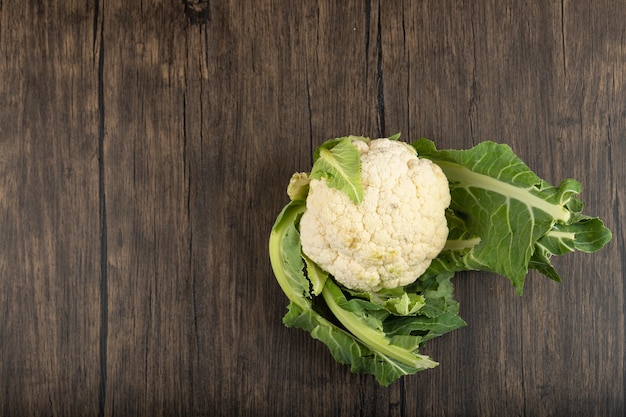 Coliflor fresca con hojas verdes colocadas sobre la superficie de madera