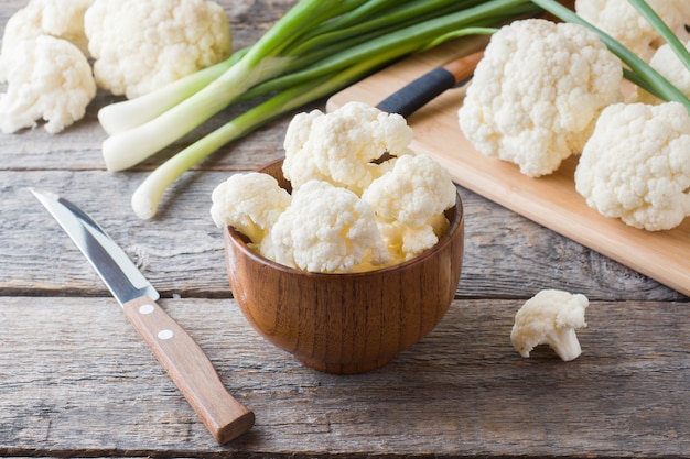 Coliflor orgánica fresca, cortada en trozos con cebolla verde y cuchillo sobre madera