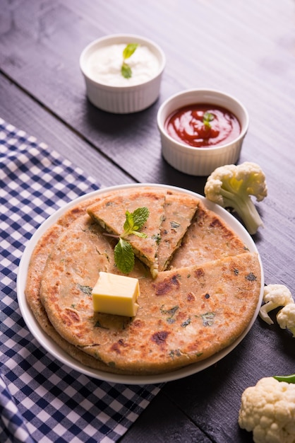 La coliflor rellena o Gobi Paratha es un pan plano indio. Menú favorito para el desayuno o el almuerzo en el norte de la India, servido sobre un fondo de mal humor con requesón y salsa de tomate en un tazón