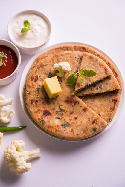 La coliflor rellena o Gobi Paratha es un pan plano indio. Menú favorito para el desayuno o el almuerzo en el norte de la India, servido sobre un fondo de mal humor con requesón y salsa de tomate en un tazón