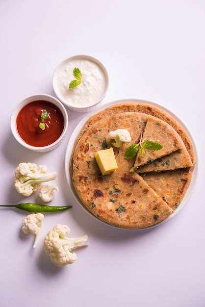 La coliflor rellena o Gobi Paratha es un pan plano indio. Menú favorito para el desayuno o el almuerzo en el norte de la India, servido sobre un fondo de mal humor con requesón y salsa de tomate en un tazón