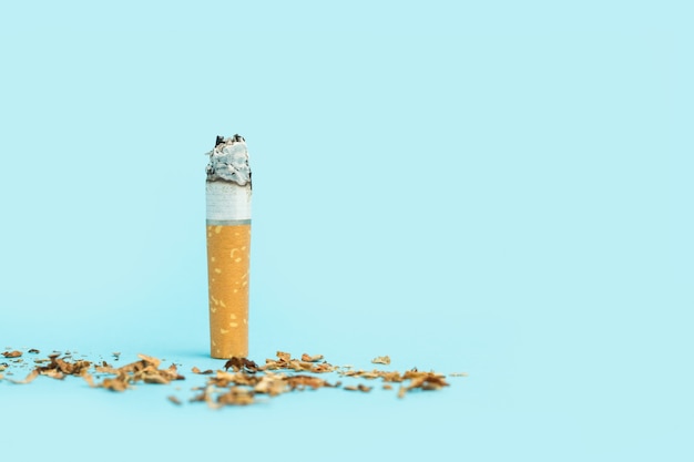 Una colilla de cigarrillo encendida sobre un fondo azul claro