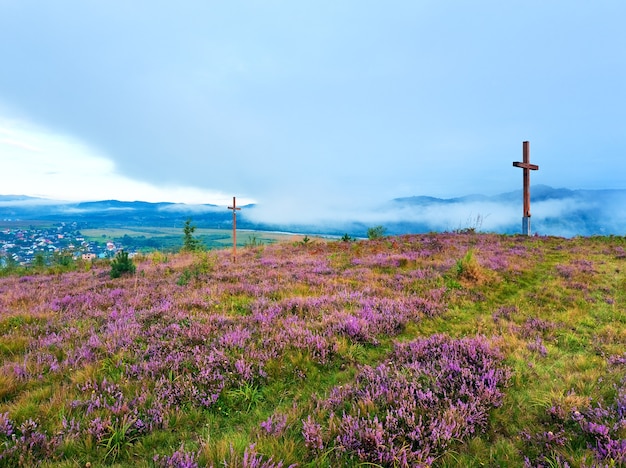 Colina de flores de brezo de verano, vista del país por la mañana brumosa detrás y cruces de madera (Óblast de Lviv, Ucrania).