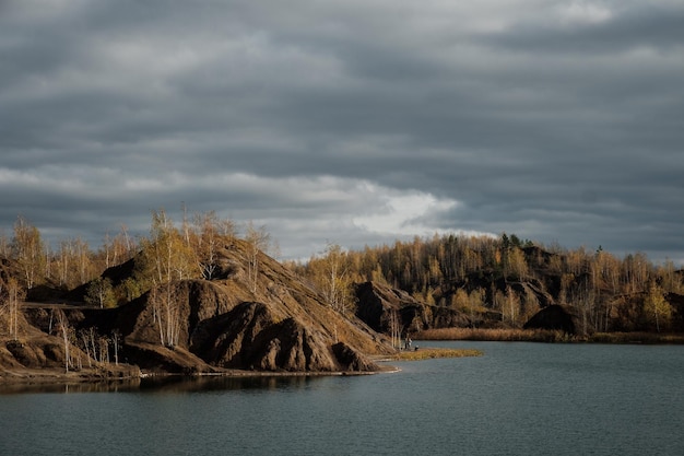 Colinas de minas de carvão abandonadas de areia marrom minas de produção de resíduos paisagem industrial no outono com bétulas amarelas contra um céu cinza