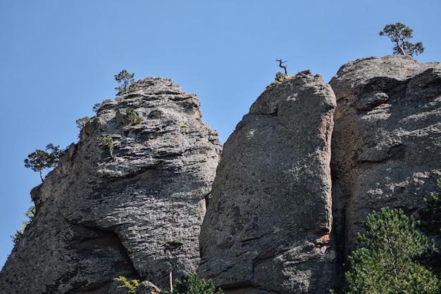 Colinas de piedra y montañas con árboles y arbustos verdes contra el cielo azul.