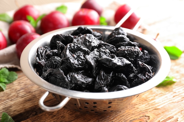 Collander con sabrosas ciruelas secas en la mesa