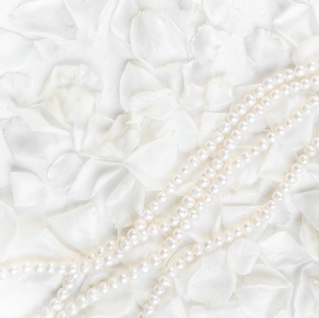 Collar de perlas sobre un fondo de pétalos de rosas blancas ideal para tarjetas de felicitación para bodas cumpleaños