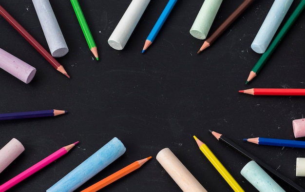 Se coloca una capa uniforme de lápices de colores en un tablero de dibujo infantil negro con una copia del espacio.