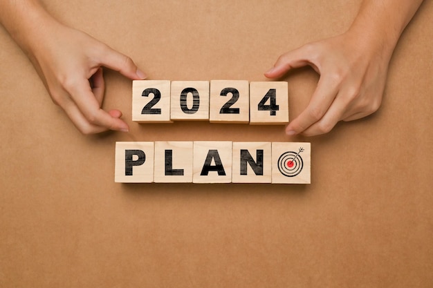 Coloca a mano cubos de madera con el PLAN 2024 sobre un fondo marrón Objetivos del plan de negocio y concepto de estrategia