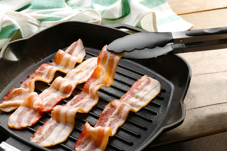 Foto coloca una rebanada de tocino en la sartén con pinzas de primer plano