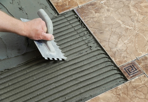 Colocação de telhas cerâmicas. Espátula adesiva em um piso de concreto como preparação para o assentamento de ladrilhos brancos.