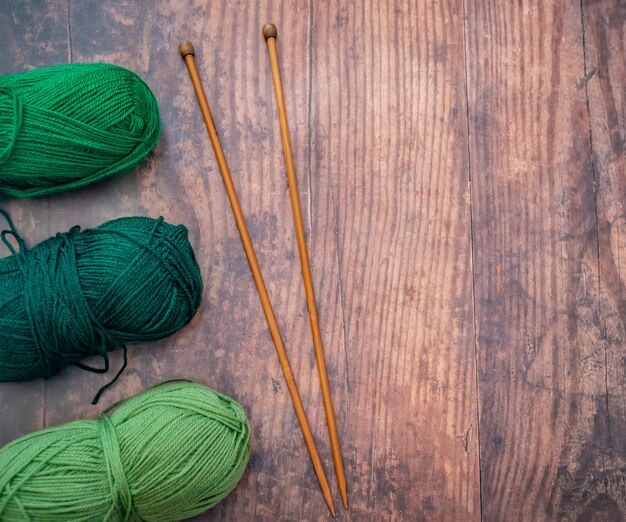 Colocação plana de bolas verdes de fio de tricô e agulhas de tricó de bambu em um chão de madeira dura