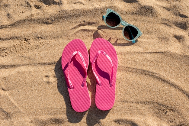 Foto colocación plana de chanclas y gafas de sol sobre arena.