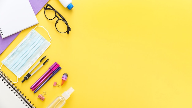 Colocación plana de materiales de regreso a la escuela con gafas y mascarilla