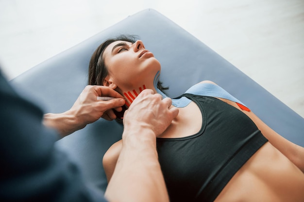 Foto colocando fita kinesio no pescoço mulher visitando fisiologista