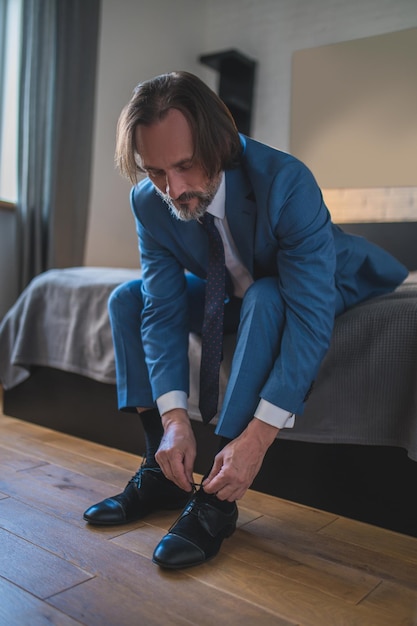 Colocando sapatos. Homem de terno azul, calçando os sapatos enquanto sentado no sofá