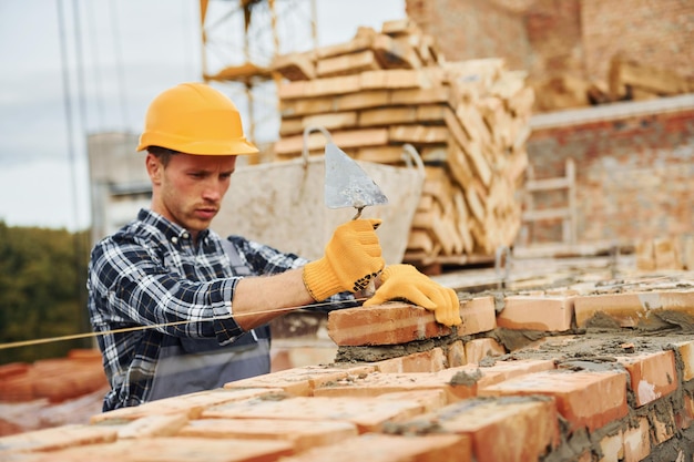 Colocando tijolos Trabalhador da construção em uniforme e equipamento de segurança tem trabalho na construção