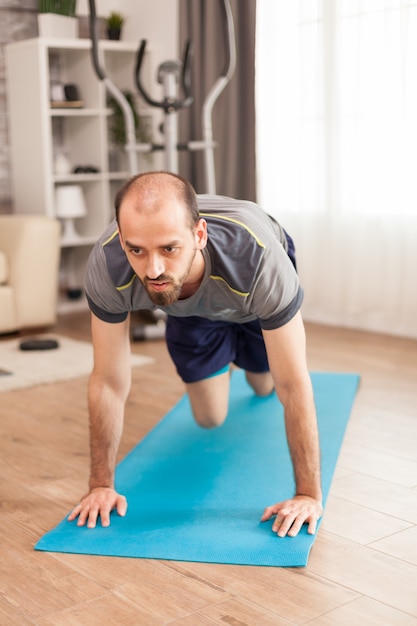 Colocar al hombre en su apartamento haciendo ejercicio de escaladores en la estera de yoga durante la pandemia mundial.