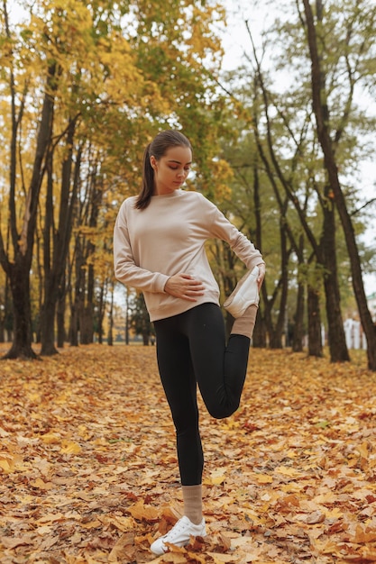 Colocar atleta femenina estirando la pierna mientras se equilibra en el camino durante el entrenamiento físico en el parque