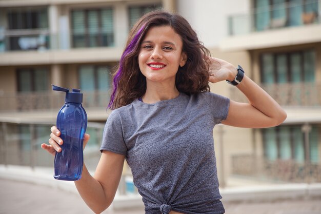 Colocar chica caucásica con botella azul en la mano de pie fuera haciendo ejercicios concepto