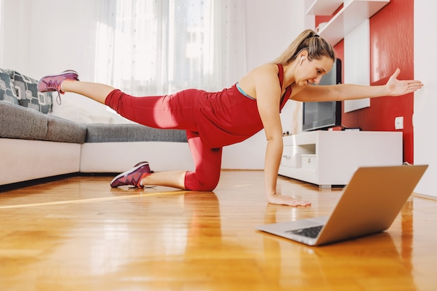 Colocar deportista arrodillada en el suelo en casa y haciendo ejercicios de fitness mientras sigue la clase online.