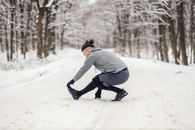 Colocar deportista haciendo ejercicios de calentamiento en un día nevado de invierno en el bosque. Fitness de invierno, vida sana