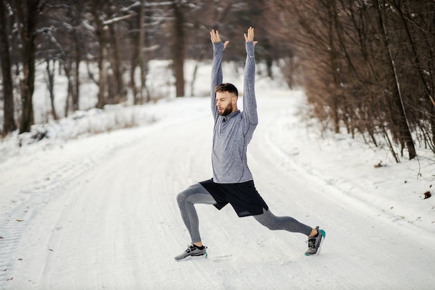 Colocar deportista haciendo ejercicios de calentamiento en la naturaleza sobre la nieve en invierno.