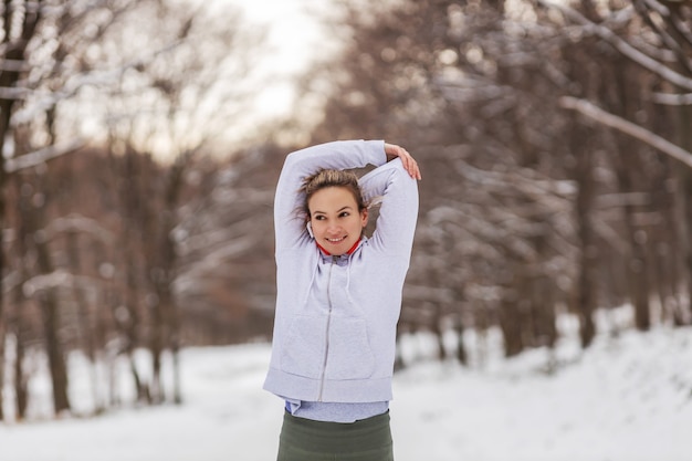 Colocar deportista de pie en la naturaleza sobre la nieve en el día de invierno y hacer ejercicios de calentamiento. Fitness de invierno, vida sana, fin de semana, libertad.