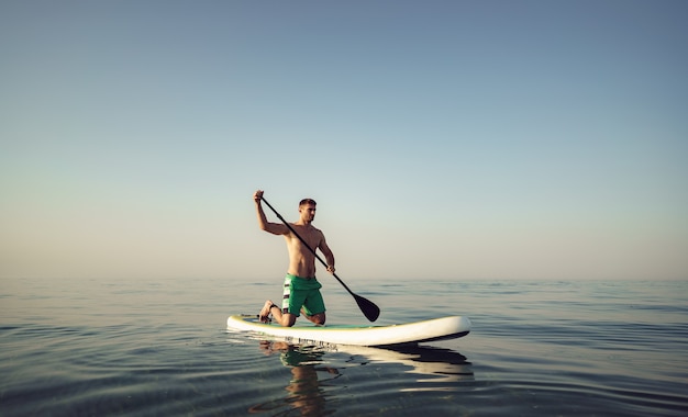 Colocar joven hombre en paddle board flotando en el lago