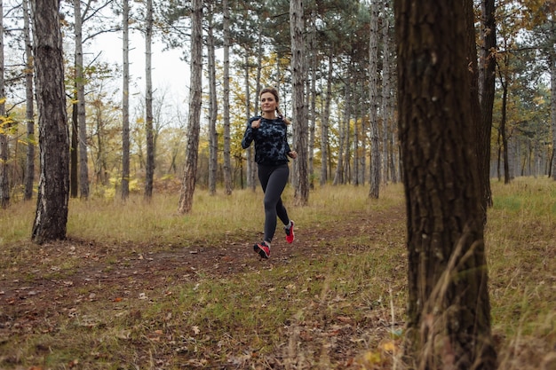 Colocar joven mujer en ropa deportiva corre a lo largo de camino forestal